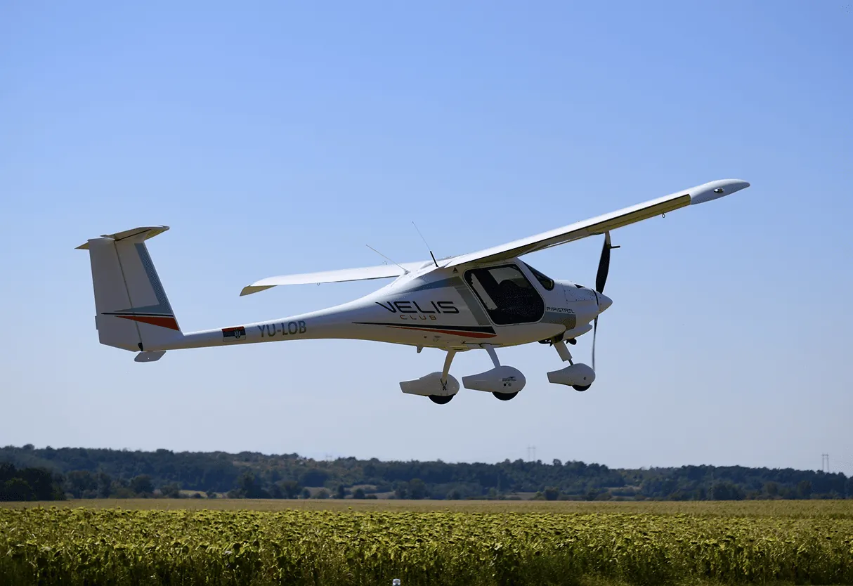White Pipistrel Velis Club training aircraft, registration YU-LOB, flying low over a sunflower field on a clear day